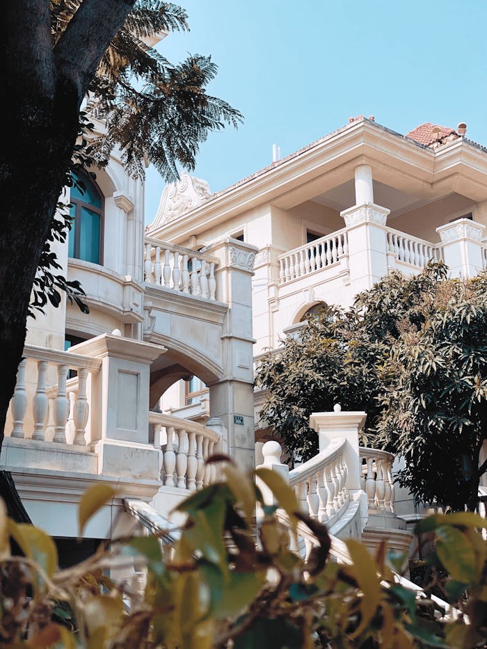 A stunning mansion featuring classical architecture with lush foliage and a clear sky.